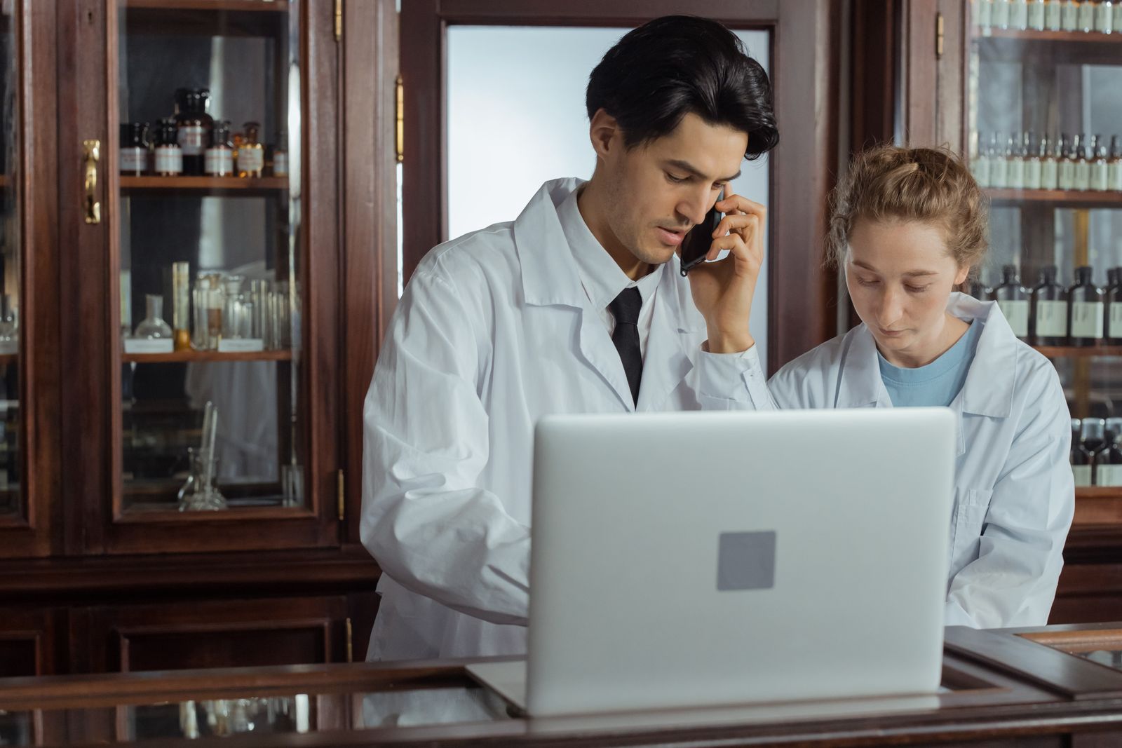 Zwei Apothekenmitarbeiter am Laptop in der Offizin, einer telefoniert